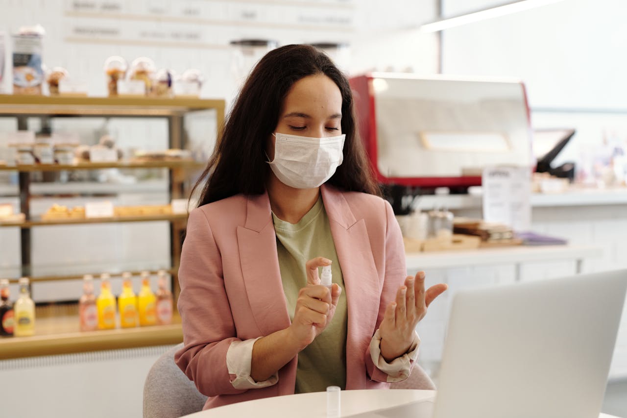 Woman wearing mask sanitizing hands in a cafe, focusing on hygiene and safety.